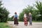 Three hippie women, wearing boho style clothes, holding guitar, walking on dirt road in countryside. Friends, traveling together
