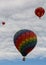 Three hot air balloons float away into a sky filled with puffy white clouds