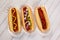 Three hot dogs on a wood table with different condiments
