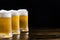 Three ice-cold beer mugs on wooden base on black background with copy space. Sselective focus