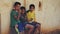 Three Indian boys sitting outdoors, eating chips and looking to the camera. INDIA, NEPAL , APRIL 2018