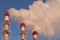 Three industrial chimneys emitting white smoke against a blue sky