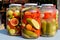 Three jars with mixed pickles on a white table for sale at a food market with pickled cucumbers, green tomatoes, red peppers, melo