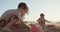 Three kids building sand castles on the beach during sunset