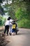 Three kids pushing motorbike on village road sloping slight uphill