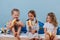 Three kids in sleeping clothes sitting on unmade bed, eating bananas