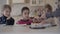 Three kids at the table with small cake and juice glasses. Hand of a woman cuts the cake and puts a piece to boy`s plate