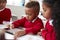 Three kindergarten school kids sitting at desk in a classroom using a tablet computer and stylus together, selective focus