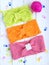 Three knitted headbands for girls: light green, orange, pink. Hair bands are on a white wooden background with hooks.