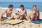 Three lads sat on beach with bodyboards