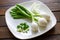 Three large Mexican onions which are green onions that have been allowed to grow bigger on a white plate with some smaller green o