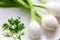 Three large Mexican onions which are green onions that have been allowed to grow bigger on a white plate with some smaller green o