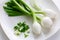 Three large Mexican onions which are green onions that have been allowed to grow bigger on a white plate with some smaller green o