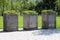 Three large old concrete outdoor flower pots filled with low growing dense green plants on top of stone tiles at local graveyard