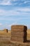 Three large rectangular haystacks made of three hay bales, placed on harvested wheat field, slightly cloudy summer blue skies