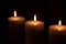 Three large white candles burn in the dark