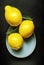 three lemons on a plate with a green leaf on top of it on a black surface with a black background