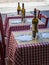 Three Little Wooden Tables Set with Red Checked Tablecloth, Wine Bottles and Cutlery