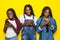 Three lovely young african girls wearing casual clothes using cell phones isolated over yellow background