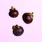 Three mangosteens floating over a pink background