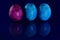 Three marbled, colored, blue and pink Easter eggs stand side by side against a reflective blue background and are reflected on the