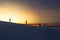 Three men descend from the mountain at sunset in winter, on a steep descent, in the distance