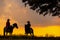 Three men dressed in cowboy garb, with horses and guns. A cowboy riding a horse in the sunset is silhouetted in black