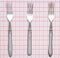 Three metal forks on a tablecloth. Top view.