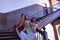 Three middle-aged Hispanic women in beautifully colored dresses with rhinestones to belly dance, posing on stairs next to a wooden