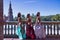 Three middle-aged Hispanic women , wearing beautifully colored dresses with rhinestones, to belly dance, posing next to a tiled