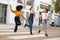 Three millennial hip girlfriends holding hands and laughing as they run across a pedestrian crossing