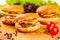 Three mini burgers with beef cutlets, tomatoes and cheese on wooden board