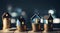 Three miniature houses atop stacked coins, symbolizing real estate investment. Bokeh background