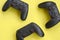 Three modern black gamepads on yellow background. Lets play video games together with friends concept. Cooperative teamplay