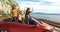 Three multi ethnic friends dancing in convertible parked with sea in background