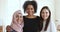 Three multicultural smiling young women friends embracing looking at camera