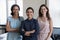 Three multiethnic businesswomen pose at workplace smile staring at camera