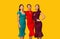 Three Multiracial Models In Dresses Standing Over Yellow Studio Background