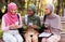 Three Muslim Students Women Using Smartphones Sitting On Bench Outdoors