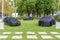 Three mystery cars are draped under black covers in a park setting