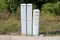 Three narrow tall plastic electrical boxes mounted on edge of asphalt backyard at abandoned industrial complex with tall grass and