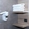 Three neatly folded white towels lie on a wooden shelf against a background of ceramic tiles.