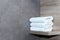 Three neatly folded white towels lie on a wooden shelf against a background of ceramic tiles.