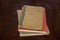 Three old discolored hardback books laying stacked on dark brown surface with foreground - bottoms of books in clear focus and