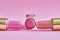 Three old used lipstick tubes lie on a pink background