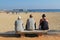 Three older men sit on a bench and looking at the sea on beach of Blanes