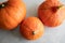 Three orange Hokkaido pumpkins of different sizes lying on a concrete gray background. Autumn