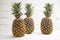 Three organic pineapple fruits on white painted wood