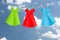 Three Origami paper dresses (green, red, blue) hanging on a clothes line in front of the blue summer sky