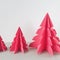 Three Origami Xmas trees, on grey table with off white background. square photo image.